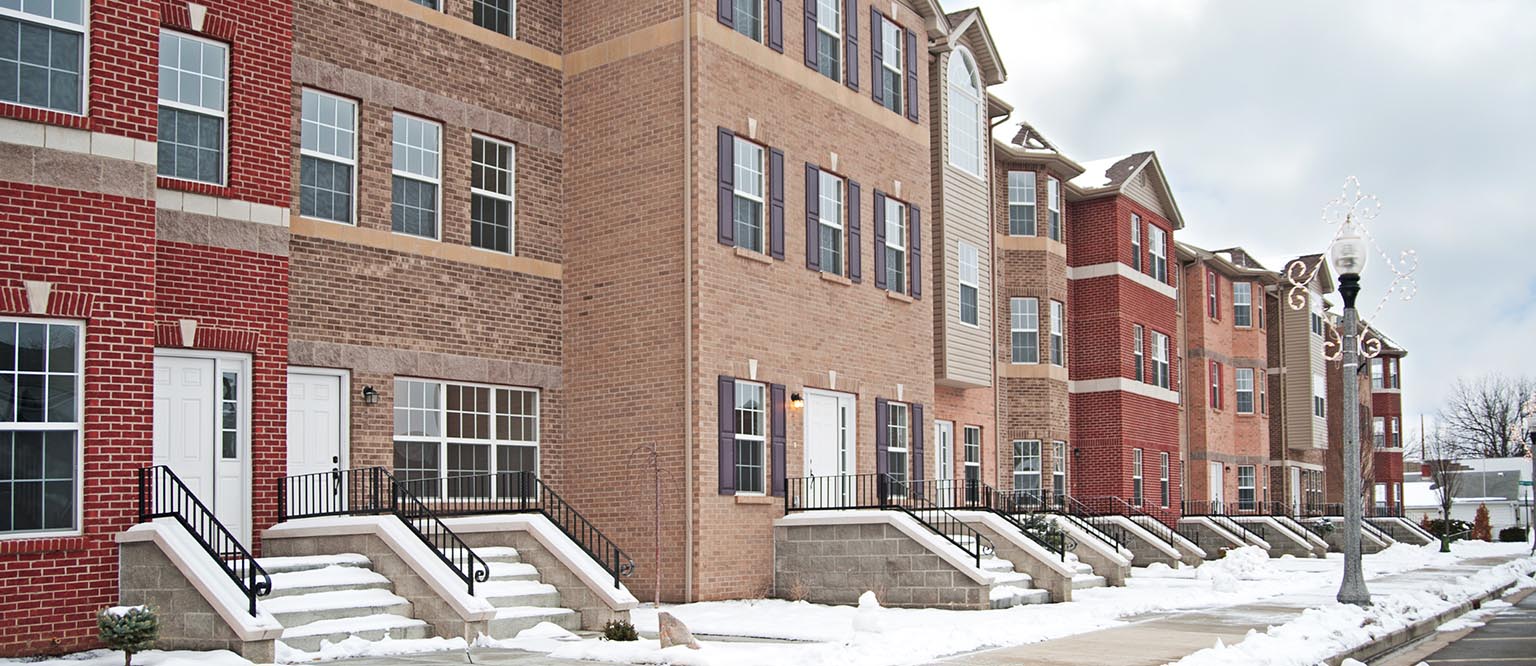 Row of brick townhouses with snow-covered sidewalks and steps in a residential neighborhood on a cloudy winter day